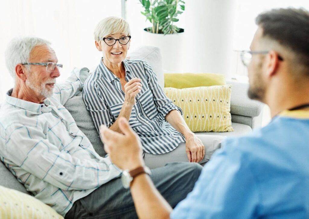 senior couple having a chat with a caregiver about rehab after surgery
