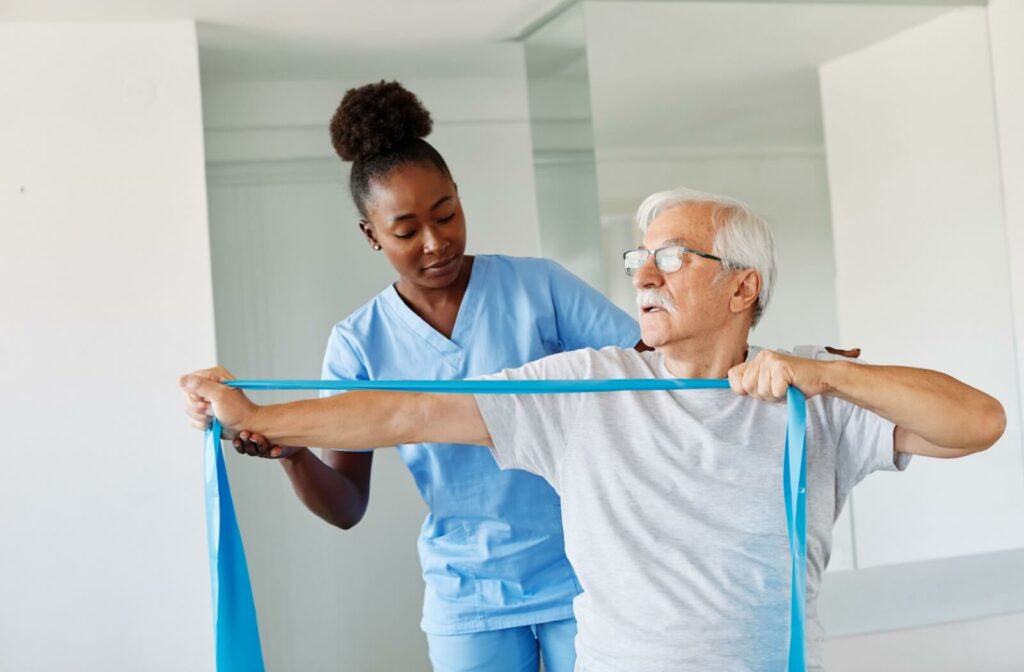 a caregiver helping a senior man exercising with a band in rehabilitiation