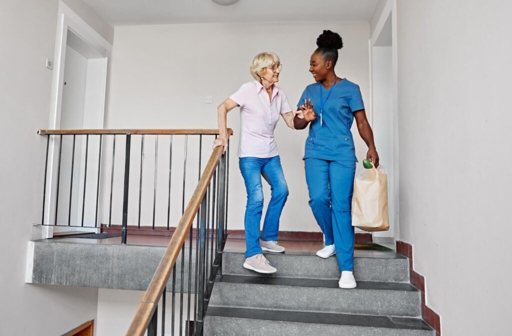 An occupational therapy assistant helps an older adult navigate the stairs of their home